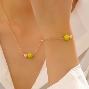 Détail des breloques cœur doré et balle de tennis sur collier et bracelet assortis