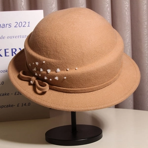 Detail of camel wool cloche hat featuring elegant white pearl flower and silk bow
