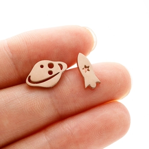 Macro shot of asymmetric rose gold spaceship and planet stud earrings on a fingertip