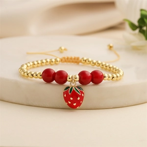 Elegant gold-beaded adjustable bracelet featuring a red enamel strawberry charm on marble stand