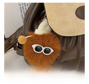 Close-up of brown plush monster keychain with white knit hat on a faux leather bag