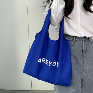 Close-up of a blue canvas tote bag featuring white AREYOU letter print on a model