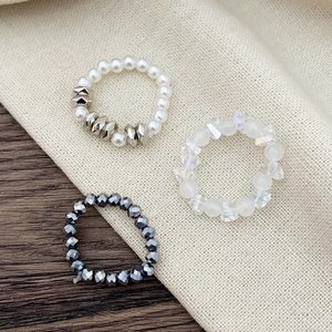 Detailed view of elastic beaded rings with pearls and metallic beads on linen background