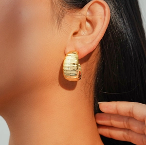 Close-up of a wide gold C-shaped earring with vertical striped texture on a model