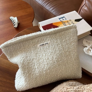 Detail of tweed weave texture and brand label on a beige wool makeup bag