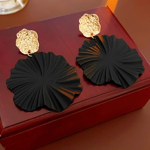Macro shot of gold hammered metal earrings with black wavy fan-shaped charms on wood