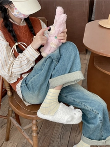 Detail showing soft white plush animal slippers and pink bunny doll in a cozy indoor setting