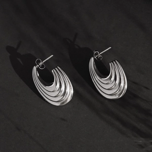 Minimalist silver steel hoop earrings with streamlined wave texture on black background