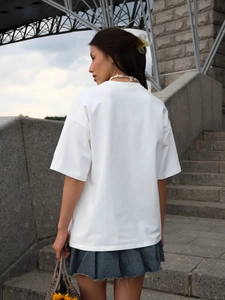 Πίσω όψη λευκού oversized βαμβακερού t-shirt σε συνδυασμό με τζιν φούστα σε εξωτερικό χώρο