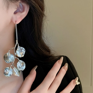 Close-up of silver leaf-shaped long drop earrings on model for a trendy metal jewelry look