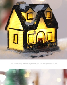 Close-up of a glowing Christmas miniature house with snow-covered roof and festive wreath