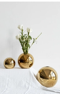 Detailed view of three polished gold spherical ceramic vases on white linen surface