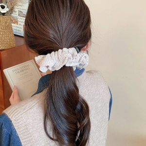 Detail of a beige knitted scrunchie with fashion label on a messy ponytail hairstyle