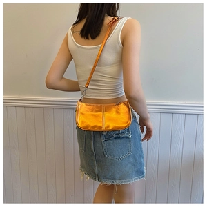 Detail view of metallic orange punk style underarm bag on model with studs and long strap