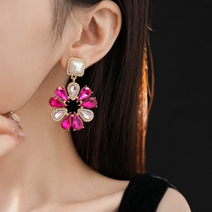Dettaglio di orecchini a fiore dorati con perle e gemme rosa indossati da una modella