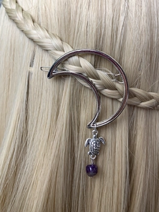Detail of silver crescent moon hair clip with turtle charm on golden braided hair