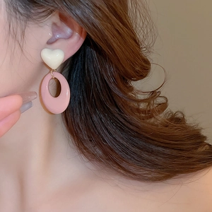Close-up of cream resin heart and pink oval geometric dangle earrings on model ear