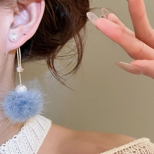 Detail of light blue fur pompom and pearl drop earrings on a model for autumn style