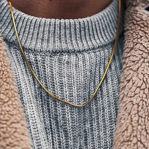 Detail view of a gold snake bone chain necklace layered on a grey knit sweater