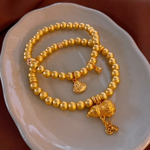 Detailed macro of gold beaded bracelets with gourd and coin charms on ceramic plate