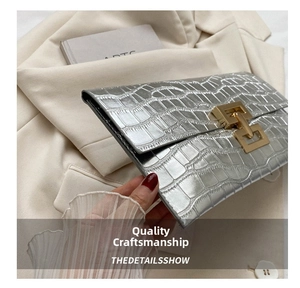 Detail of silver crocodile-embossed envelope clutch with gold metallic buckle and flap