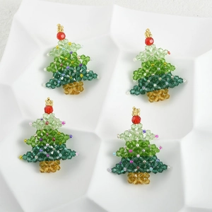 Detailed view of four handmade beaded Christmas tree charms on a white textured plate