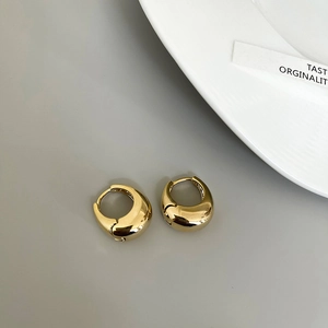 Close-up of polished gold-plated drop earrings on a minimalist grey background