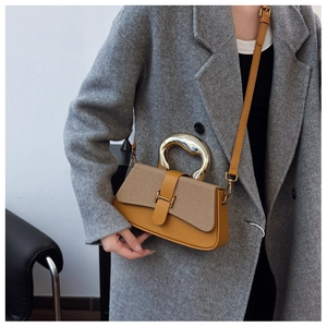 Detail of yellow leather crossbody bag with artistic gold handle worn with a grey coat