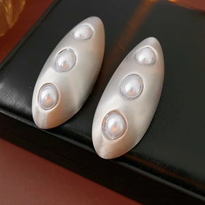 Gros plan de boucles d'oreilles ovales en argent brossé avec trois perles verticales