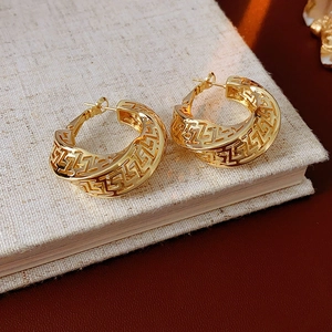 Detailed close-up of golden hollow geometric hoop earrings with Greek key pattern