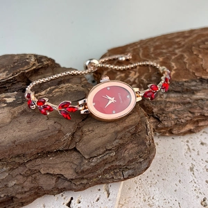 Detail of elegant gold bracelet watch with oval red dial and leaf charms on stone