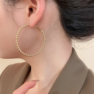 Detail of model wearing large gold twisted hoop earrings with a textured rope design
