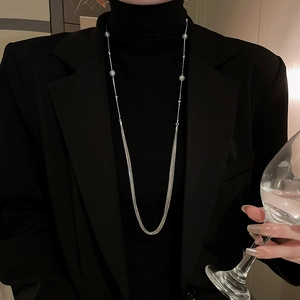 Detail of layered silver long necklace with pearls worn over a black sweater and blazer