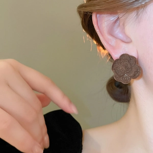 Close-up of vintage brown flocked flower stud earring on ear with floral texture
