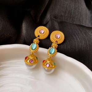 Detail of vintage gold earrings with colorful gems and pearl drops on a ceramic plate