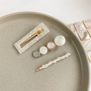 Detailed set of three golden pearl hair clips on a speckled beige ceramic tray