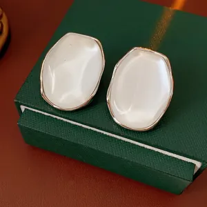 Minimalist oval resin stud earrings with gold metal frame on a green jewelry box