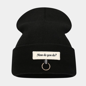 Détail du bonnet noir avec écusson 'How do you do?' et accessoire d'anneau métallique