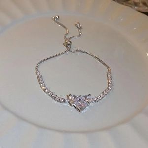 Detail of silver heart-shaped zircon bracelet with adjustable slider clasp on white plate