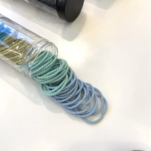 Detail of woven fabric hair ties in pastel green and blue shades spilling from a tube