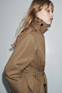 Detail of khaki trench coat featuring high stand collar with black decorative button