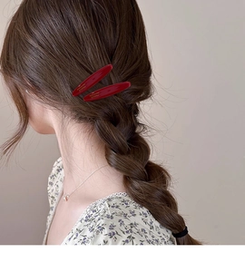 Détail de deux barrettes en acétate rouge avec lettrage doré sur des cheveux châtains