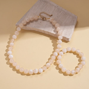 Detail of cream acrylic beaded necklace with gold lobster clasp on natural stone background