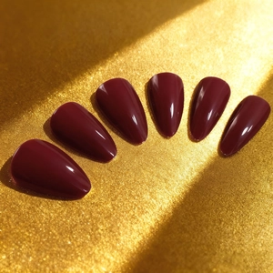 Faux ongles longs amande rouge bordeaux brillant sur tissu doré de luxe élégant