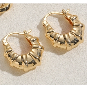 Detail shot of golden croissant textured hoop earrings on a minimalist beige background