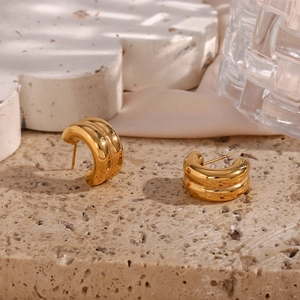 Macro view of gold-plated double-layered C-shaped hoop earrings with textured stripes