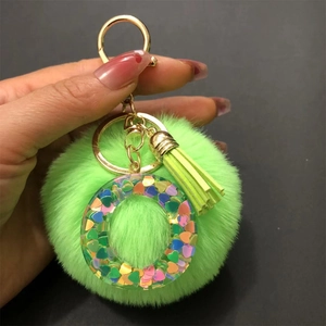 Detail of green faux fur pompom keychain with resin letter O filled with heart sequins