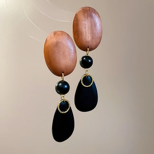 Macro detail of retro drop earrings with oval wood studs and black waterdrop charms