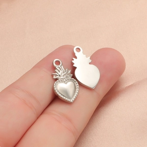 Detailed close-up of a silver sacred heart and shield charm held by hand on pink fabric