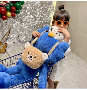 Detail of a brown fluffy teddy bear crossbody bag worn by a child with a blue plush toy